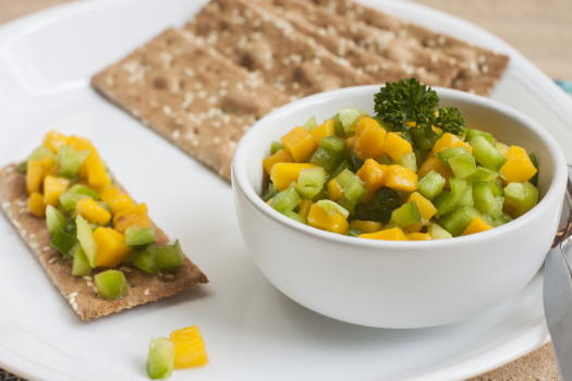 Small bowl of mango salsa on a plate of whole grain crackers